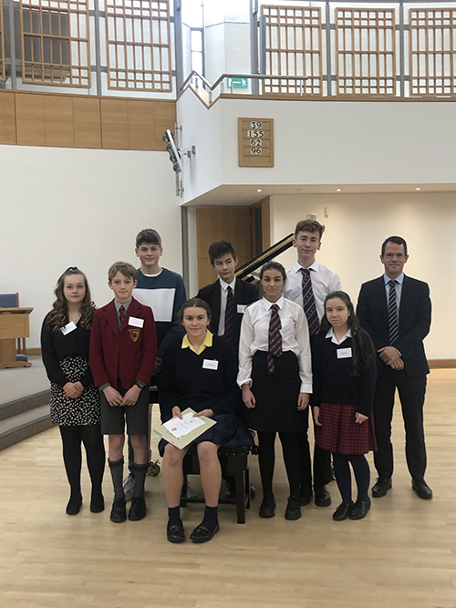 A group of student in front of a piano with their instructor